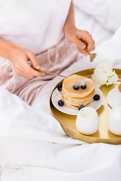 Cropped view of cutlery in hands of woman near pancakes with berries on bed on blurred background  - Φωτογραφία, εικόνα