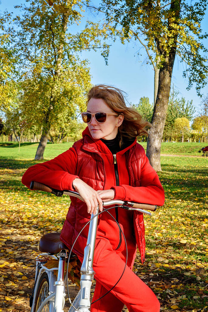 Boldog nő juharfalevéllel egy őszi parkban piros kezeslábasban. - Fotó, kép