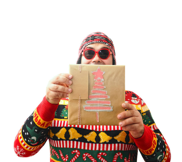 Funny man in knitted hat hiding face behind Christmas gift box and looking at camera during holiday celebration. isolated on white background - Foto, imagen