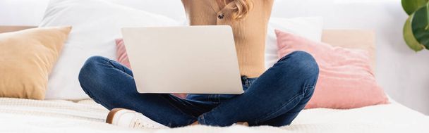Cropped view of woman with crossed legs holding laptop on bed, banner  - Photo, Image