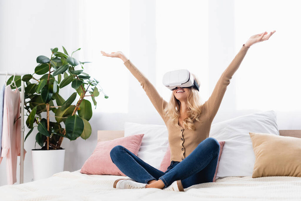 Smiling woman in vr headset sitting on bed at home  - Photo, Image