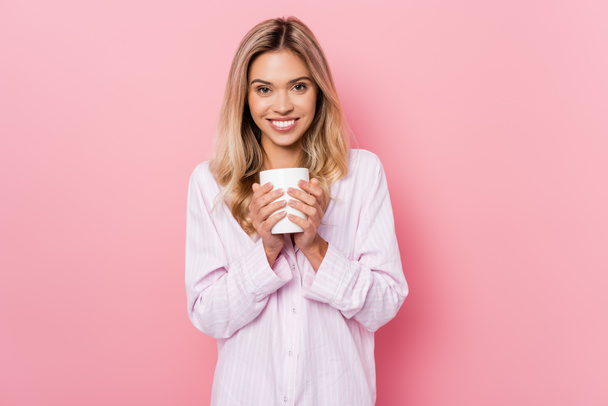 Cheerful woman in pajamas holding cup on pink background - Photo, Image