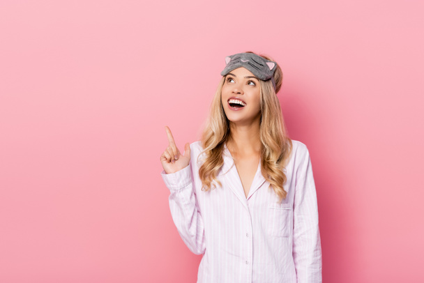 Excited woman in blindfold and pajamas pointing with finger at pink background - Fotografie, Obrázek
