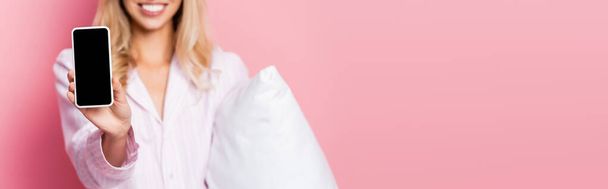 Widok na smartfona z pustym ekranem w dłoni uśmiechnięta kobieta z poduszką na różowym tle, baner  - Zdjęcie, obraz