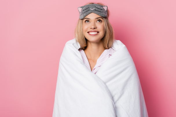 Χαμογελαστή γυναίκα με δεμένα μάτια και κουβέρτα κοιτάζοντας πάνω σε ροζ φόντο - Φωτογραφία, εικόνα