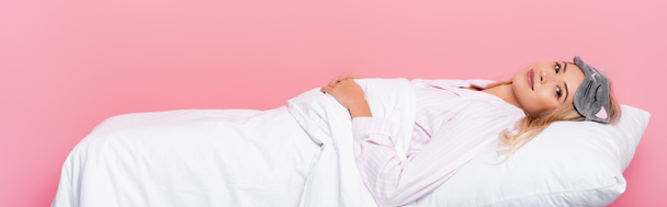 Mladá žena v pyžamu ležící na polštáři s dekou na růžovém pozadí, prapor  - Fotografie, Obrázek
