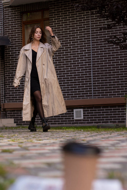 atrakcyjna szczupła brunetka w płaszczu moda i czarny strój chodzenia w kierunku. Jesień, żółte liście. ceglany budynek - Zdjęcie, obraz
