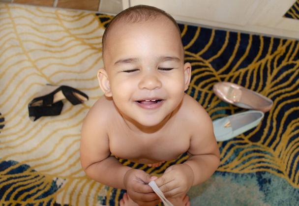 幸せな1歳の赤ちゃんの目のカメラの前で閉じて笑っている。乱雑な部屋で幼児を笑っています。子供と一緒に家にいる - 写真・画像