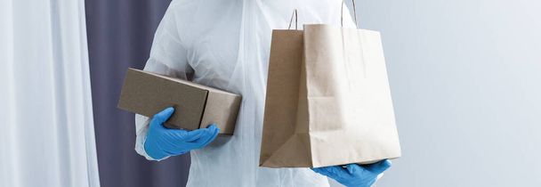 Açık gri arka planda karton kutulu kimyasal koruyucu elbise giyen bir adam. Coronavirüs salgını - Fotoğraf, Görsel