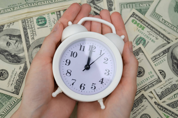 Naisten kädet valkoinen herätyskello taustalla dollarin seteleitä lähikuva. Rahoituksen käsite, liiketoiminta - Valokuva, kuva