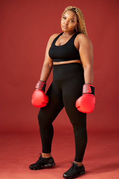 african oversize woman with red boxing mitts isolated on red background - Foto, afbeelding