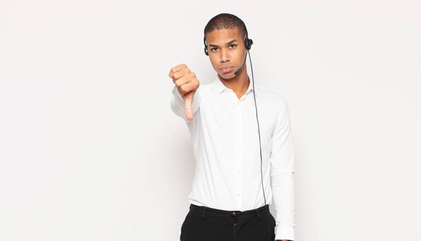 νεαρός μαύρος άνδρας αισθάνεται θυμωμένος, ενοχλημένος, απογοητευμένος ή δυσαρεστημένος, δείχνοντας τους αντίχειρες κάτω με ένα σοβαρό βλέμμα - Φωτογραφία, εικόνα