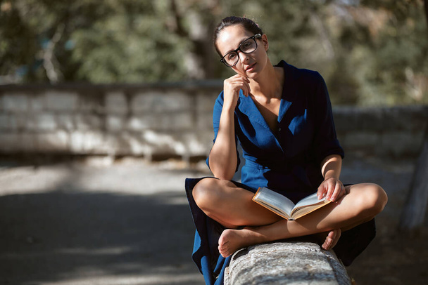 Mulher inteligente em óculos sentado ao ar livre no parque com livro. Leia livro, estilo de rua e conceito de caminhada na cidade, espaço de cópia - Foto, Imagem
