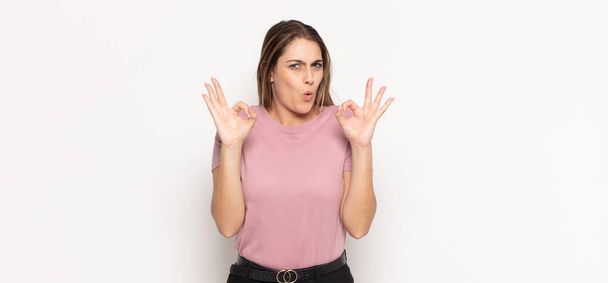 young blonde woman feeling shocked, amazed and surprised, showing approval making okay sign with both hands - Fotoğraf, Görsel