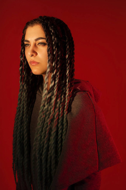 Attractive girl with dreadlocks. Red background. - Фото, изображение