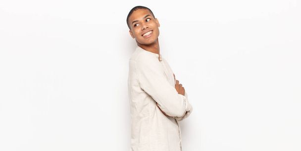 young black man smiling gleefully, feeling happy, satisfied and relaxed, with crossed arms and looking to the side - Foto, imagen