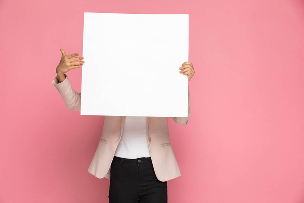üzletasszony bemutató üres hirdetőtábla, amely eltakarja arcát rózsaszín háttér - Fotó, kép