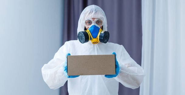 Man in protective suit, a mask and a respirator. Holds a box - Photo, Image