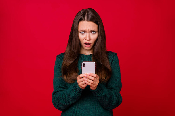 Photo de fille étonnée lire x-mas post sur son téléphone portable porter pull vert isolé sur fond de couleur rouge brillant - Photo, image