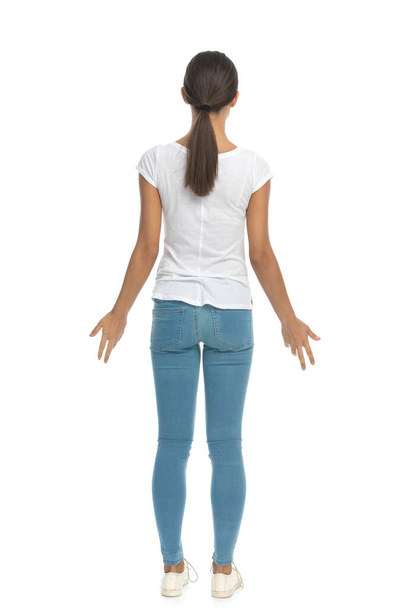 Vista posterior de la mujer casual siendo sorprendido, de pie sobre fondo de estudio blanco - Foto, Imagen