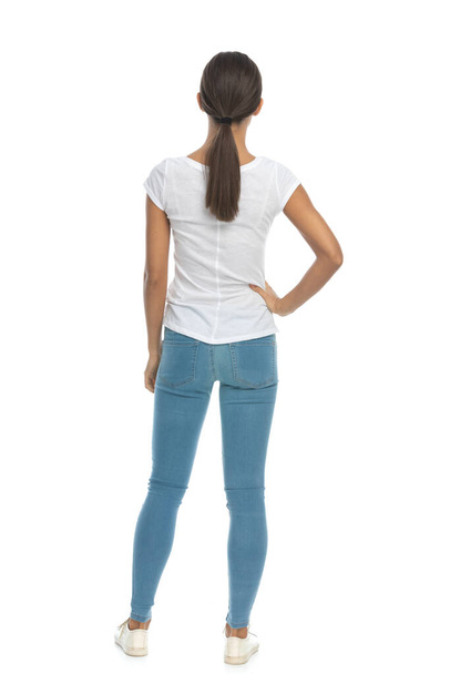 Vista posterior de la mujer casual sosteniendo la mano oh cadera mientras está de pie sobre fondo blanco estudio - Foto, Imagen