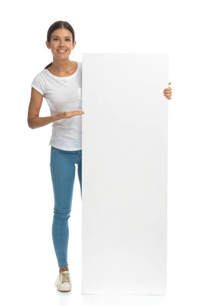 Positive casual woman presenting blank billboard while standing on white studio background - Foto, imagen