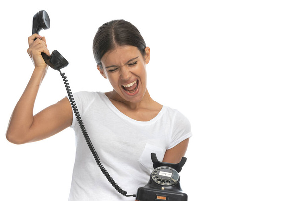 Radosna, swobodna kobieta rozmawiająca przez stary telefon i krzycząca stojąc na białym tle studia - Zdjęcie, obraz