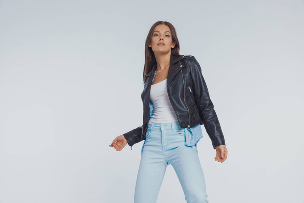 Charming fashion model wearing leather jacket while standing on gray studio background - Foto, Imagem