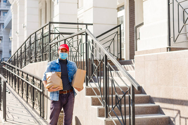 Evin arka kapısında beyaz bir yemek poşeti taşıyan bir teslimatçı. Koruyucu maskeli bir yemek dağıtıcısı. - Fotoğraf, Görsel