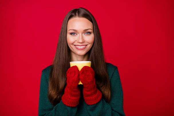Фото позитивной девушки держать чашку горячего кофе в шерстяных варежках изолированы на ярко-красном фоне - Фото, изображение