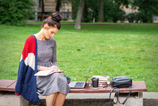 Étudiante jeune femme écrit des notes pour journal intime sur le banc dans le parc - Photo, image
