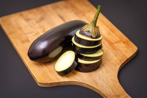 Fresh sliced eggplant on wooden cutting board isolated on black. Cooking ingredients - Fotó, kép