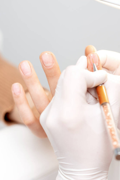 Profesyonel manikür ustası genç bir kadının tırnağına pembe jel kalemle süslemeler çiziyor. - Fotoğraf, Görsel