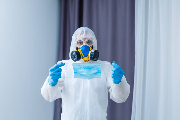 薄いグレーの背景に段ボール箱付きの化学保護スーツを着た男。コロナウイルスの発生 - 写真・画像