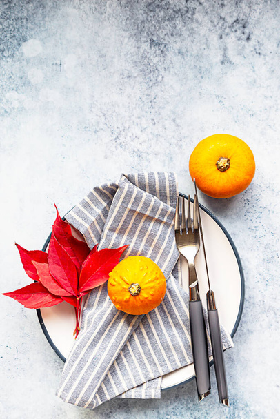 Autumn table setting. Mini decorative pumpkin, autumn red leaves, fork and knife on light blue concrete background. Top view. Copy space. - Fotografie, Obrázek