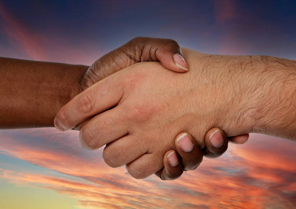 Handshake between two hands with different colors on a amazing sky of background - Photo, Image