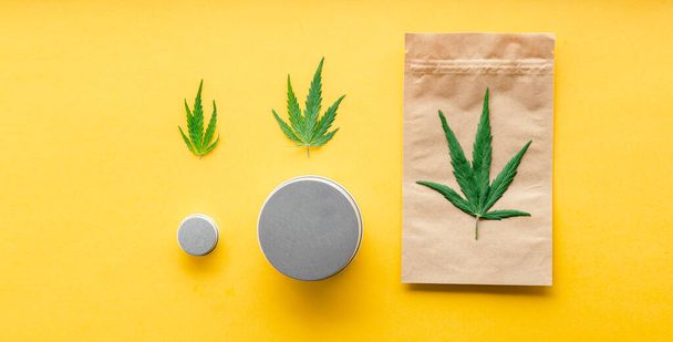 Craft package with cannabis leaf and metal jars. Different sizes of Cannabis Packages, weed trade legalization. Pharmacy drugs medical marijuana long web banner on yellow background. - Фото, зображення