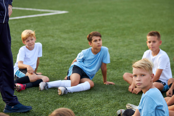 group of happy caucasianteen boys in football uniforms having a rest on the sport field - 写真・画像