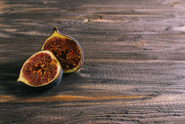 two halves of fresh figs on an old dark dark wood table. Copy space on a dark background. - Φωτογραφία, εικόνα