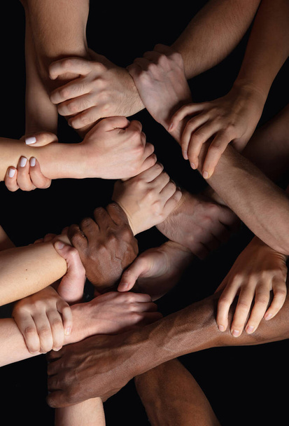 Las manos de la gente se agolpan en contacto aisladas en el fondo negro del estudio. Concepto de relación humana, comunidad, unidad, simbolismo - Foto, imagen