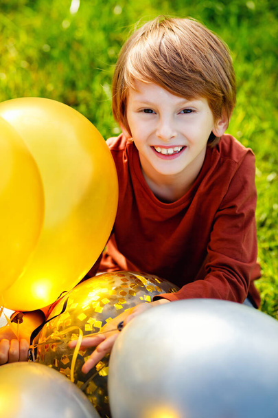 Молодий рудий хлопчик грає з купою жовтих білих чорних куль в парку
. - Фото, зображення