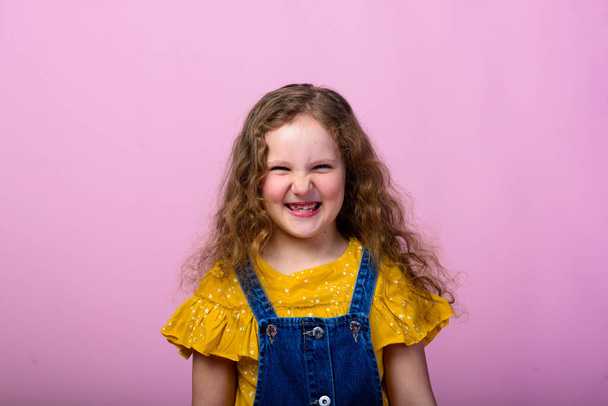 Felices emociones infantiles despreocupadas. Energetic alegre adorable niña riéndose de broma sobre fondo rosa en el estudio. - Foto, Imagen