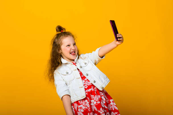 Bébé fille heureuse avec téléphone isolé sur fond jaune - Photo, image