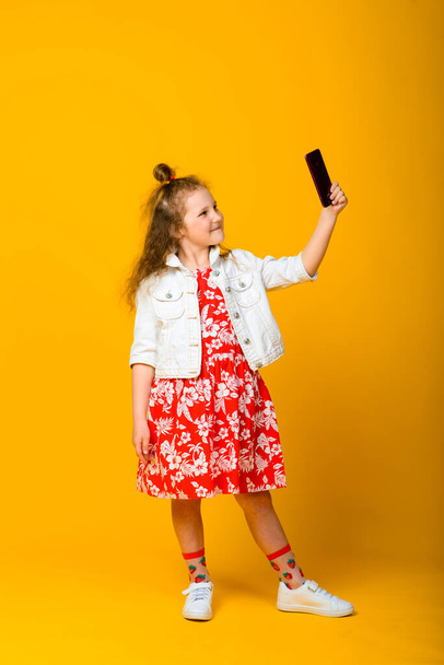 Ευτυχισμένο κοριτσάκι με το τηλέφωνο απομονωμένο σε κίτρινο φόντο - Φωτογραφία, εικόνα