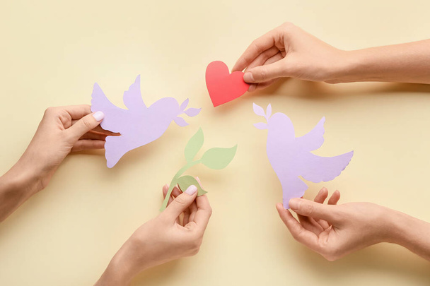 Samičí ruce s papírovými holubicemi, olivovou ratolestí a srdcem na barevném pozadí. Mezinárodní den míru - Fotografie, Obrázek