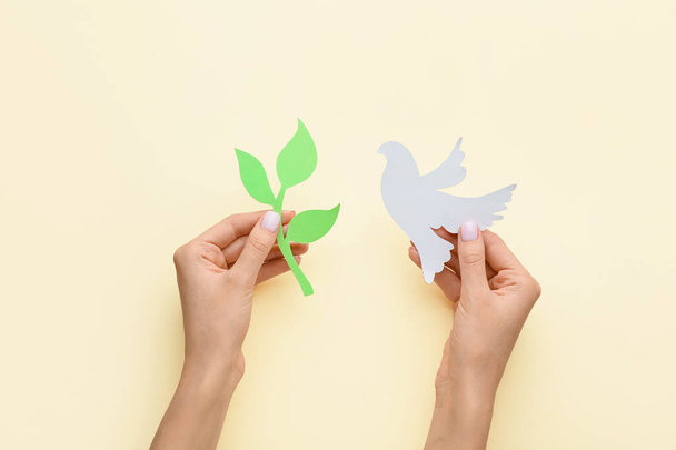 Female hands with paper dove and olive branch on color background. International Day of Peace - 写真・画像