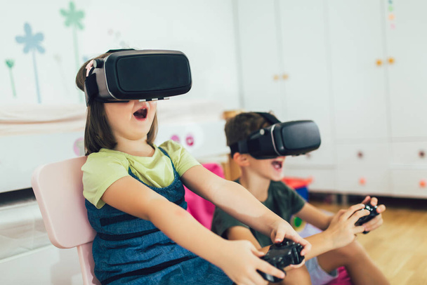 Μικρά παιδιά σε ακουστικά εικονικής πραγματικότητας που παίζουν βιντεοπαιχνίδια στο σπίτι - Φωτογραφία, εικόνα