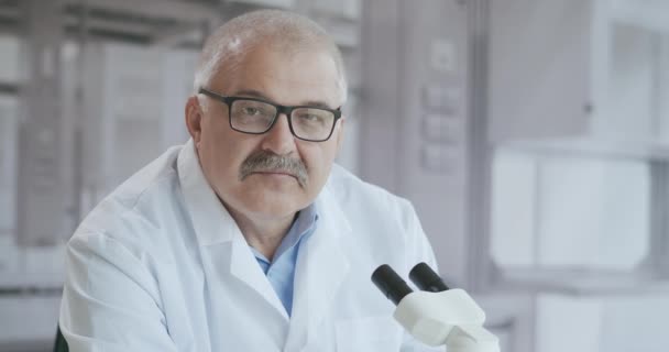 Портрет білого волосатого лікаря лабораторії з мікроскопом дивиться на камеру серйозно, а потім посміхається в повільному русі
 - Кадри, відео