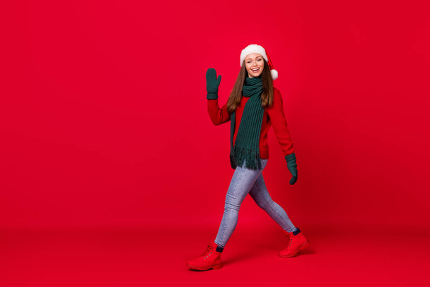 Full length body size profile side view of her she nice attractive cheerful glad girl wearing festal cap walking waving hi hello isolated over bright vivid shine vibrant red color background - Photo, image