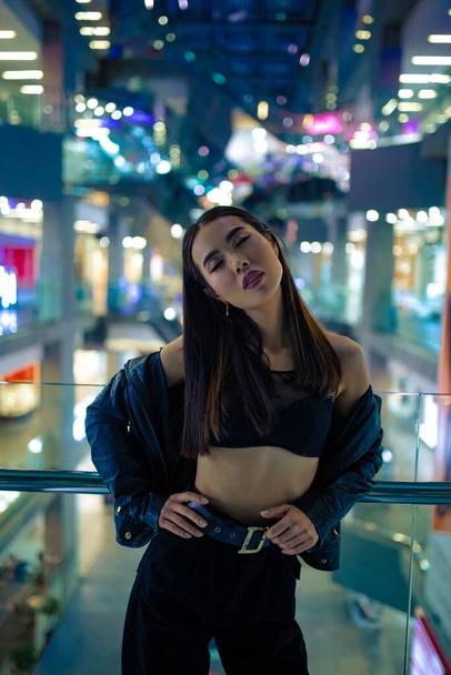 Jonge aziatische vrouw poseert in beha en jas in winkelcentrum tegen verlichting achtergrond. - Foto, afbeelding